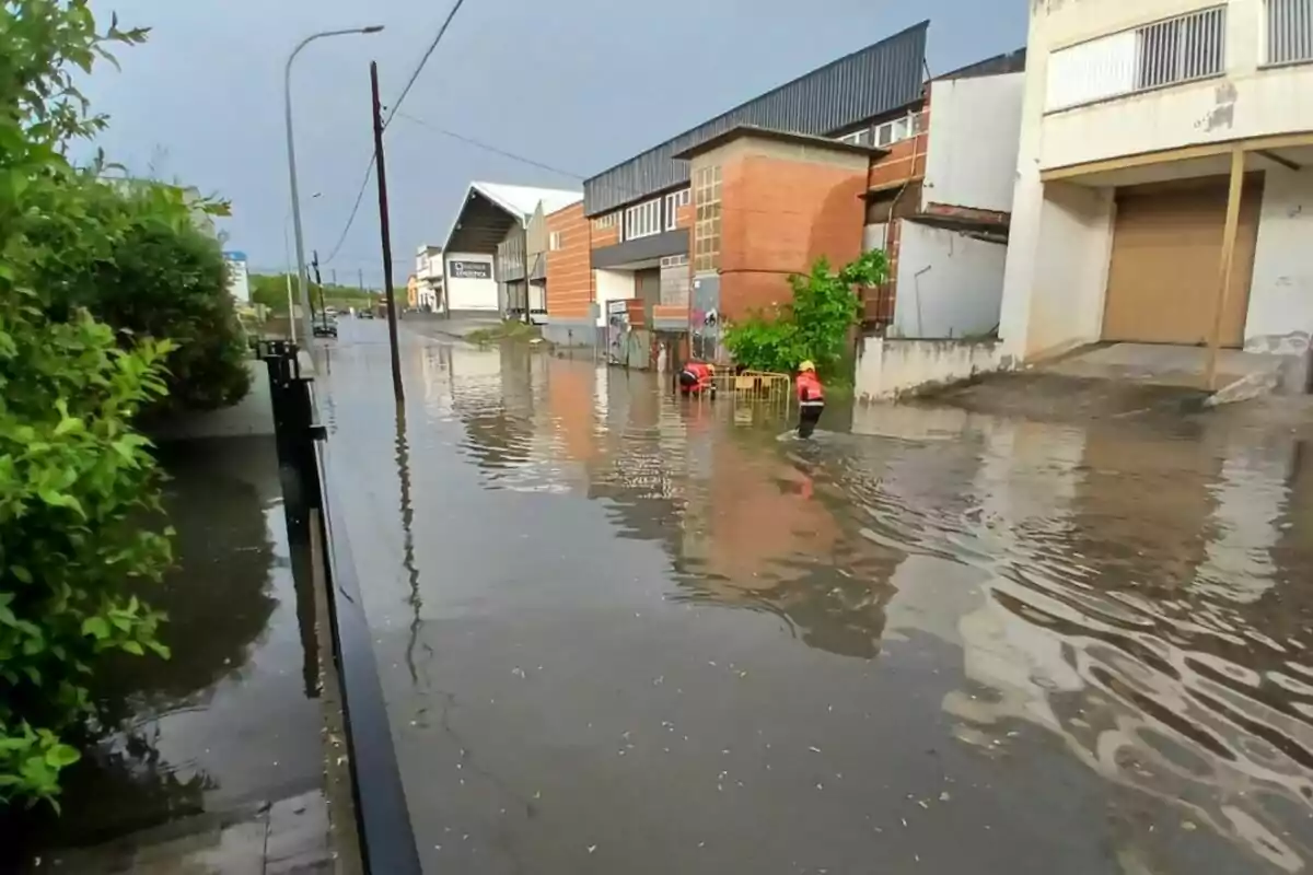 Un carrer inundat amb dues persones treballant a l'aigua davant d'edificis industrials.