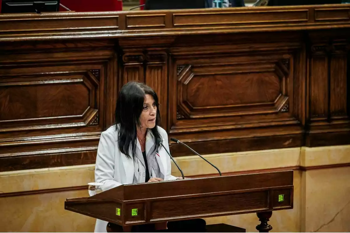 Dona de cabells foscos parlant en un faristol de fusta en un recinte parlamentari Dona de cabells foscos parlant en un faristol de fusta en un recinte parlamentari