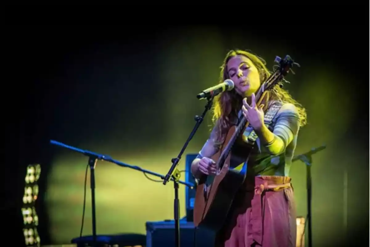 Sandra Bautista tocant la guitarra i cantant en un escenari il·luminat amb llums verdes.