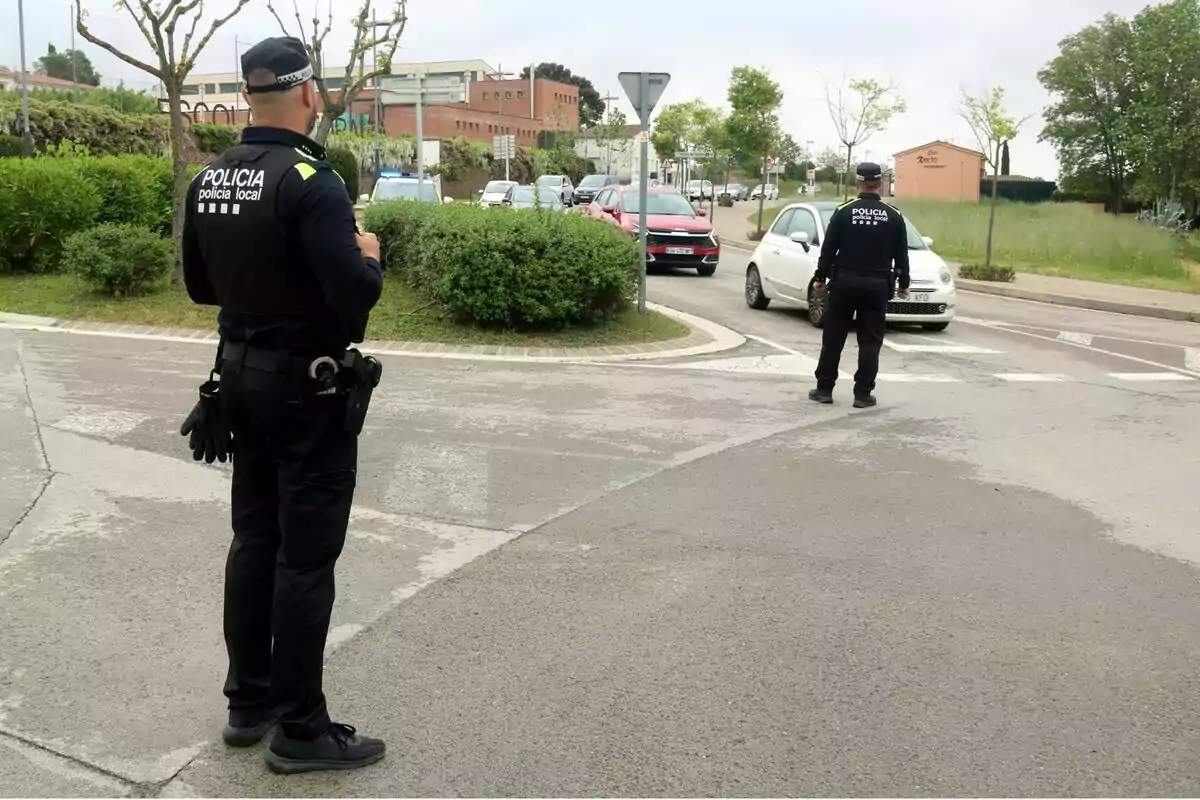 Dos policías locales están de pie en una intersección controlando el tráfico mientras varios coches pasan por la carretera. Dos policías locales están de pie en una intersección controlando el tráfico mientras varios coches pasan por la carretera.