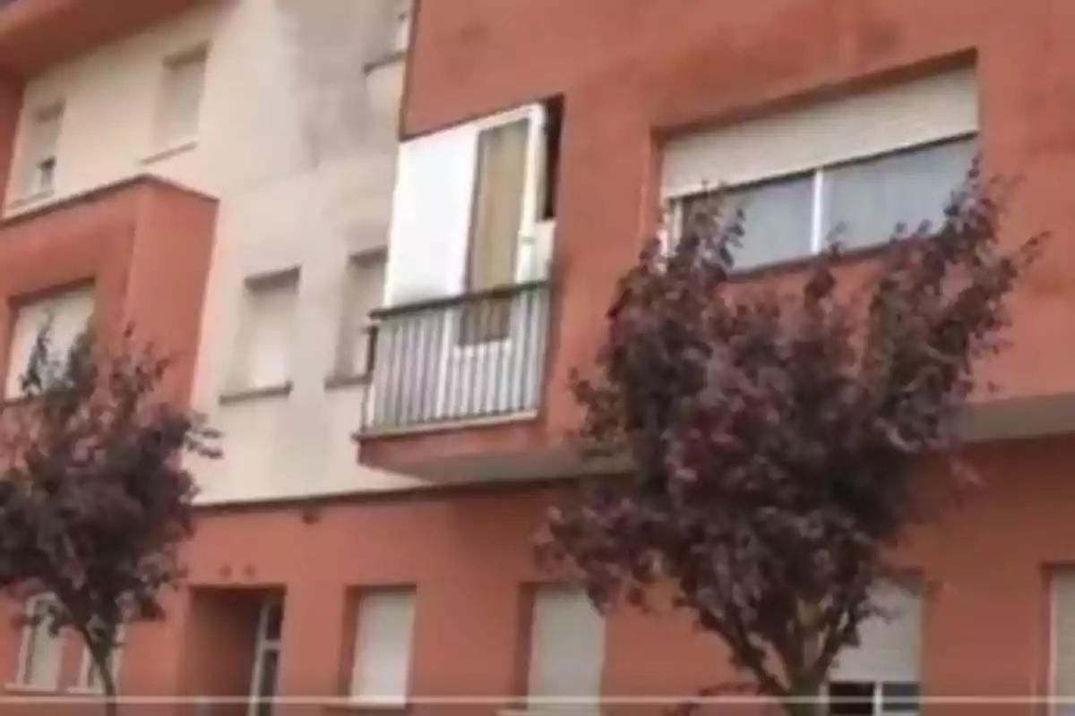 Edificio de apartamentos de ladrillo rojo con balcones y árboles en la acera.