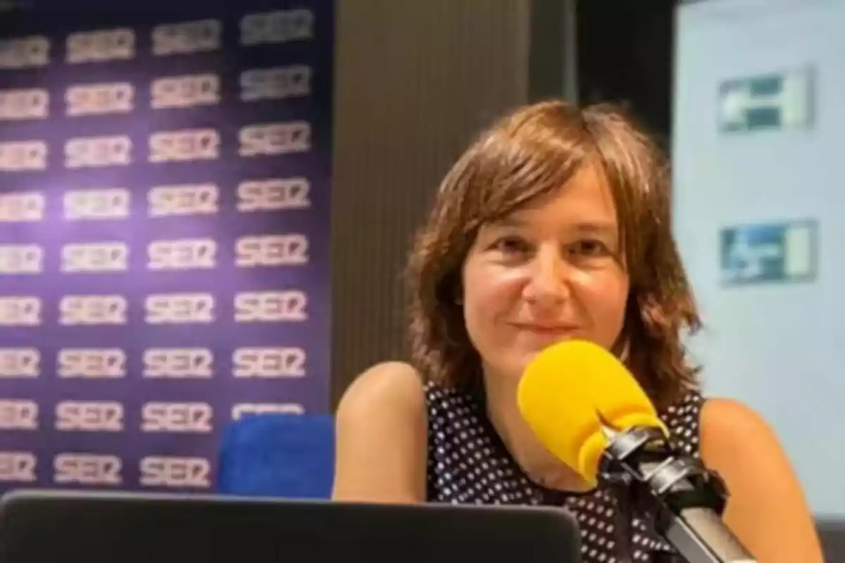 Persona parlant en un micròfon groc en un estudi de ràdio amb el logotip de la cadena SER al fons.