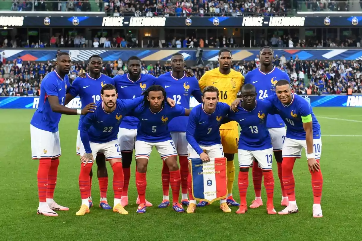 Jugadors de la selecció de futbol de França posant per a una foto grupal al camp abans d'un partit contra Luxemburg, amb el públic i el marcador de fons.