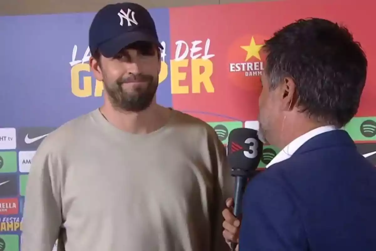 Un hombre con gorra de los Yankees siendo entrevistado por un reportero con un micrófono de TV3 frente a un fondo publicitario.