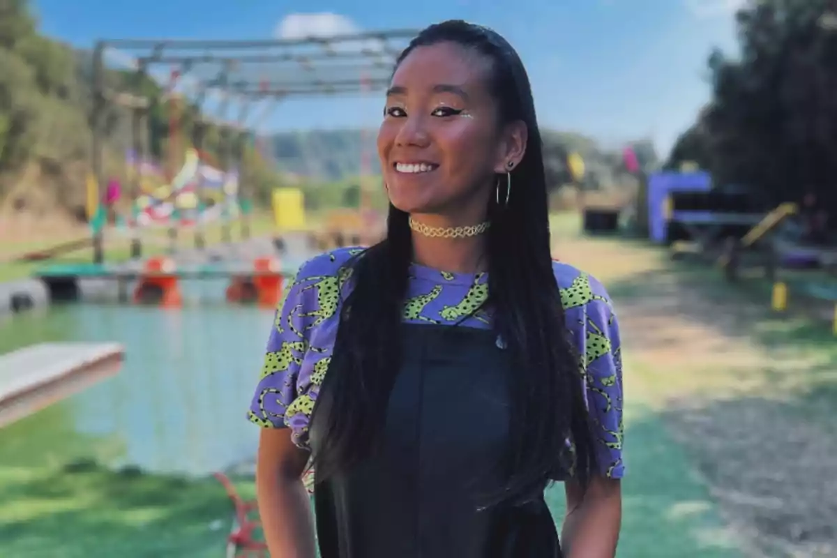 Una persona sonriendo al aire libre con un fondo colorido y un lago.