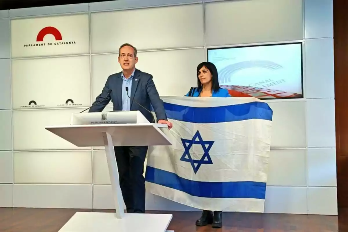 Un home i una dona en un podi al Parlament de Catalunya, la dona sosté una bandera d'Israel. Un home i una dona en un podi al Parlament de Catalunya, la dona sosté una bandera d'Israel.