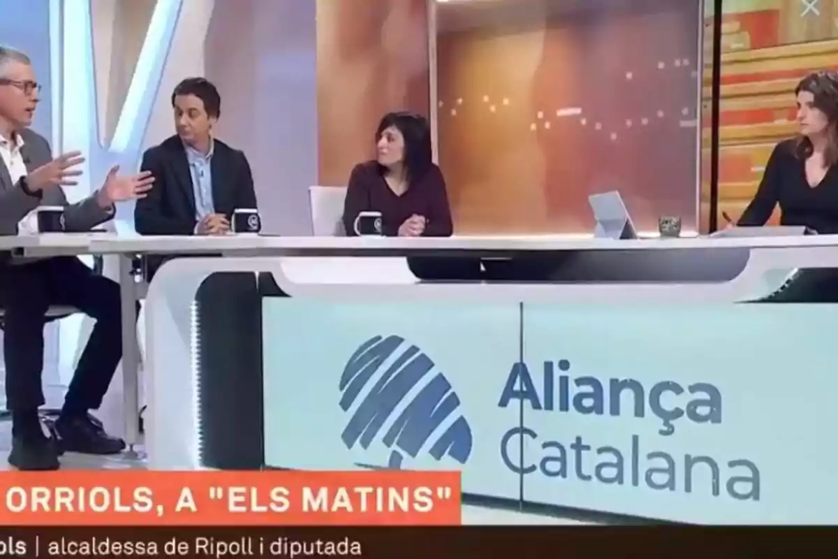 Un grup de persones participa en un programa de televisió anomenat "Els Matins" amb un cartell d'"Aliança Catalana" visible al plató.