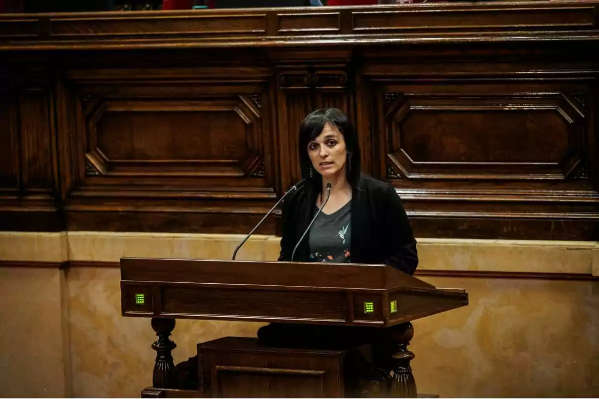 Una persona parlant en un faristol de fusta en un entorn formal.