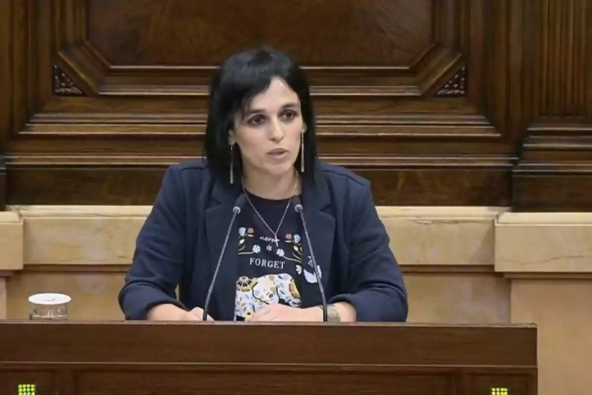 Una dona parlant en un podi de fusta amb dos micròfons.