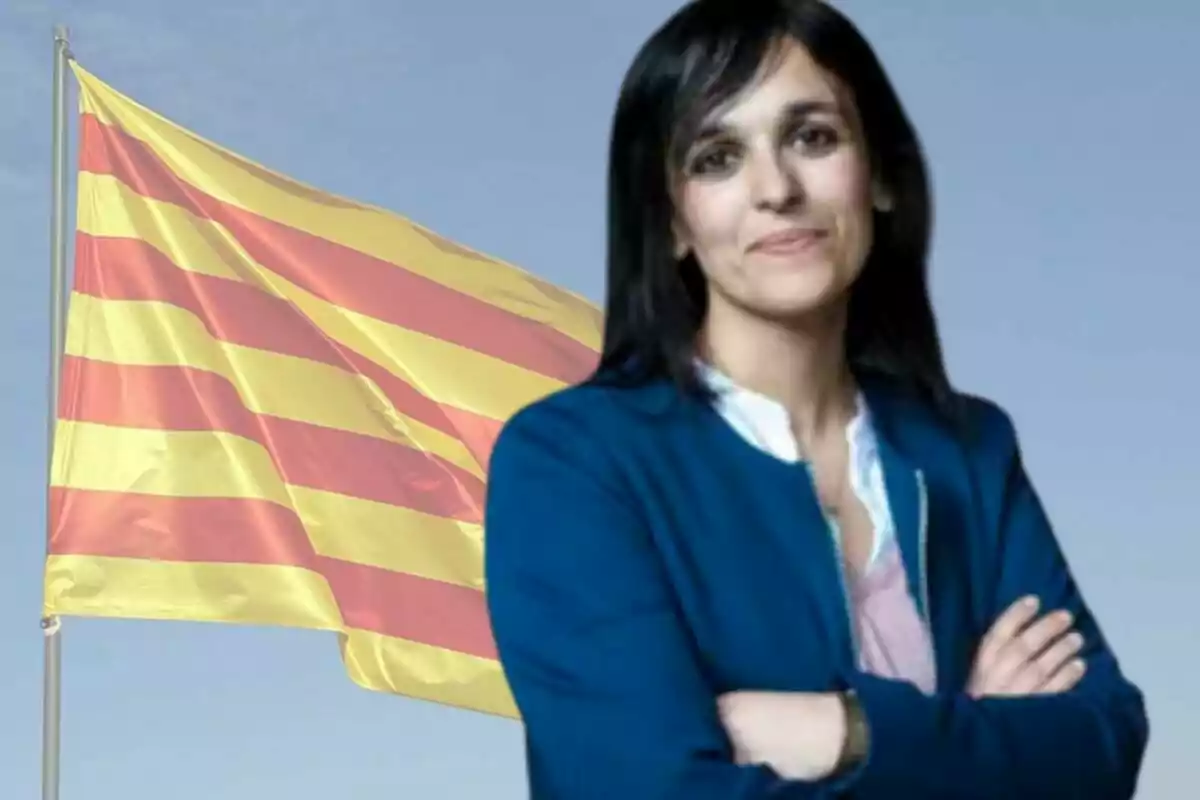 Dona de cabell fosc amb jaqueta blava davant d'una bandera catalana onejant.