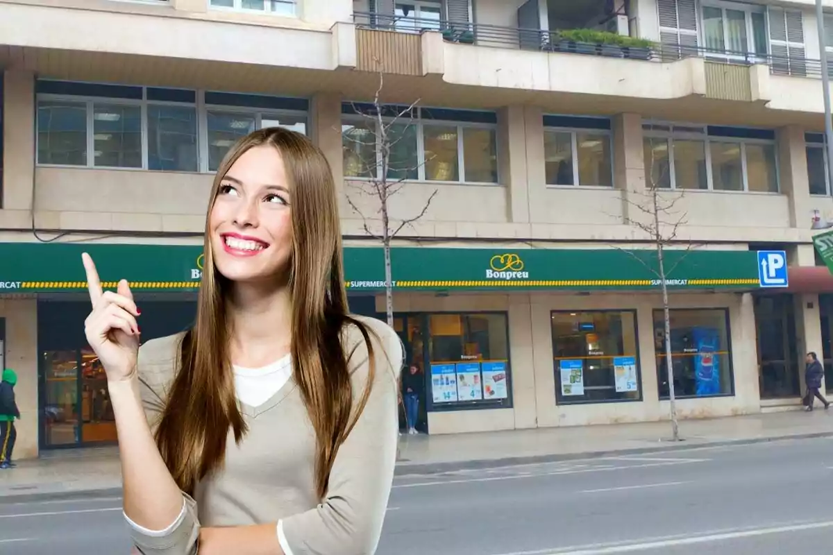 Mujer sonriendo y señalando con el dedo índice hacia arriba frente a un edificio con un supermercado Bonpreu.