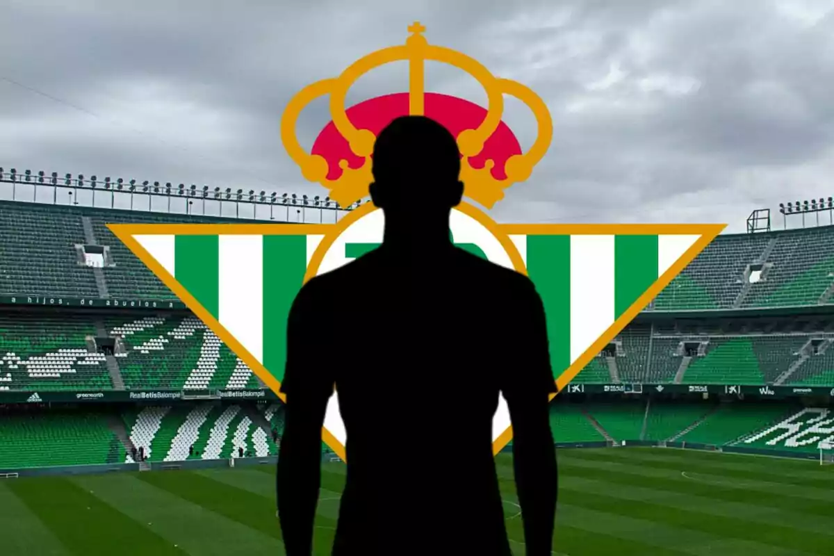 Silueta de un jugador de fútbol frente al escudo del Real Betis Balompié en un estadio vacío.