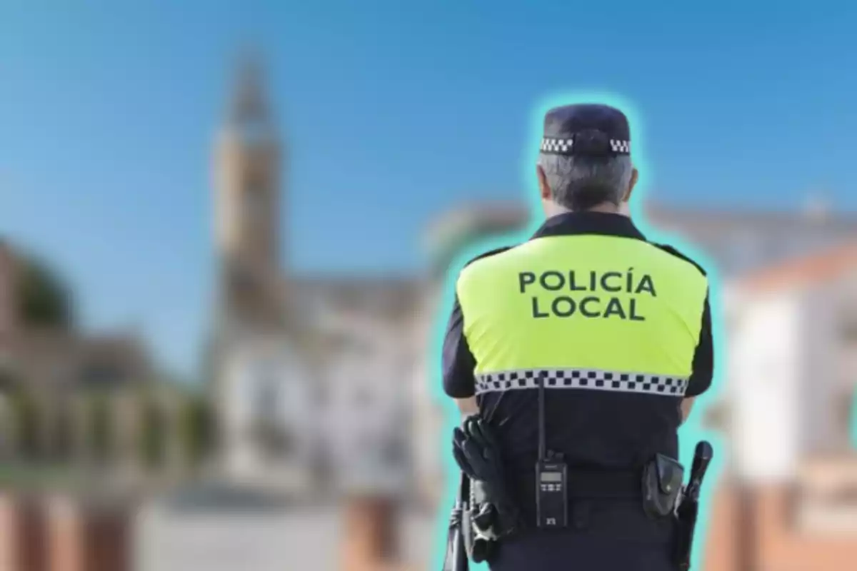 Un agent de la policia local d?esquena amb una armilla groga fluorescent i un fons urbà desenfocat.