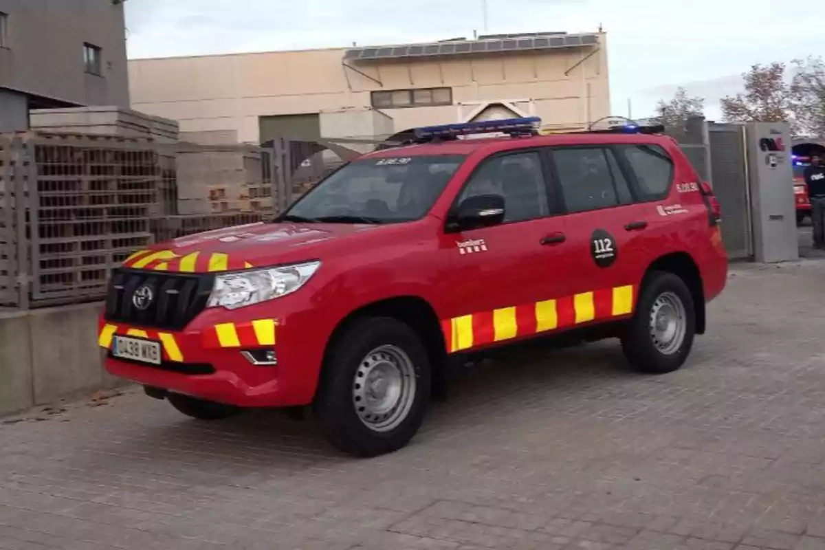 Un vehicle d?emergència vermell amb franges grogues estacionat en una àrea industrial.