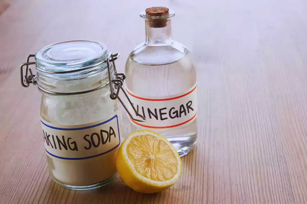 Un frasco de bicarbonato de sodio, una botella de vinagre y medio limón sobre una mesa de madera.