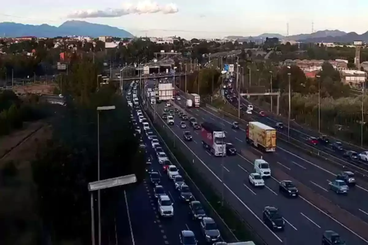 Una carretera amb trànsit dens en tots dos sentits envoltada d'arbres i muntanyes al fons.