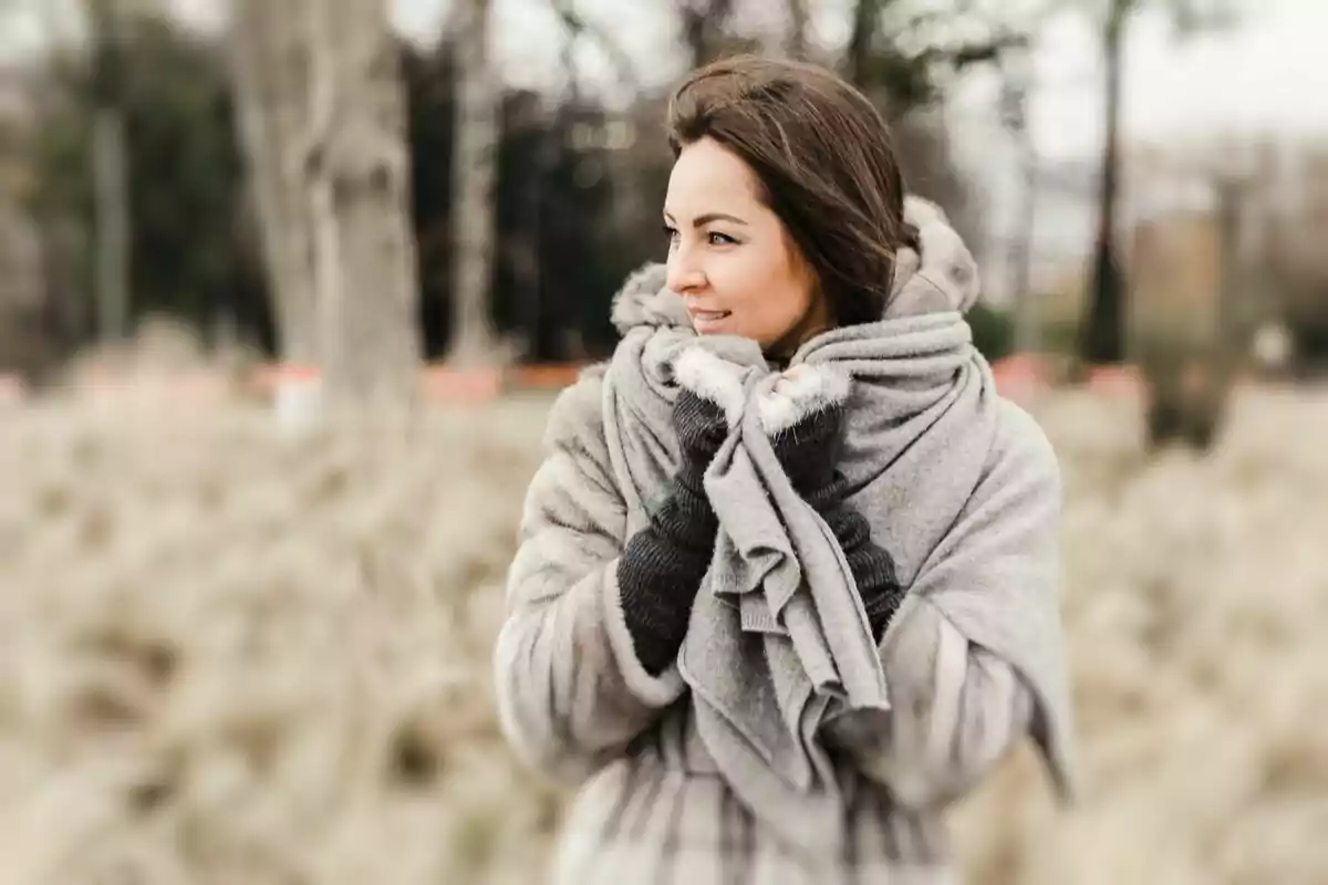 Mujer abrigada con bufanda y guantes en un entorno natural invernal.