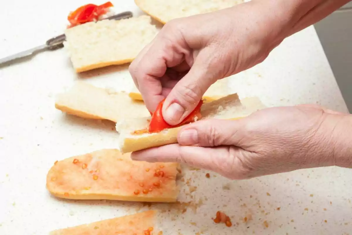 Manos preparando pan con tomate.