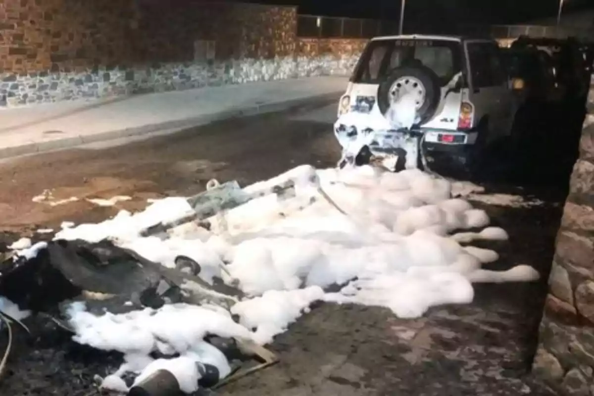 Un coche blanco con espuma de extintor en la parte trasera y en el suelo en una calle de noche.