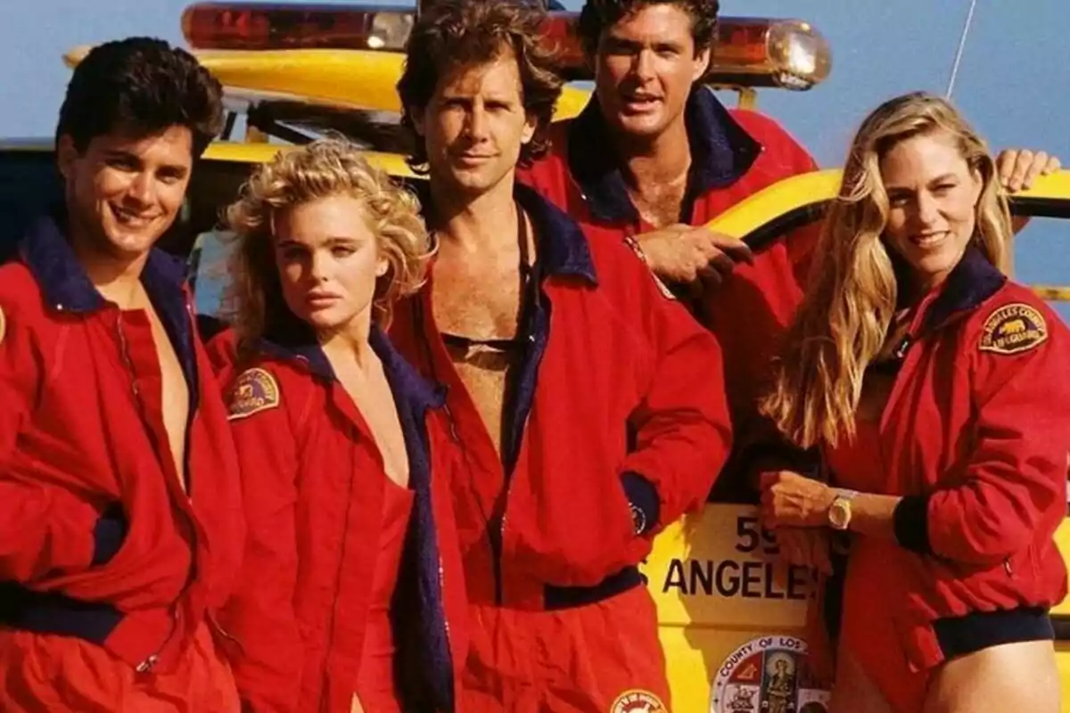 Un grupo de personas con chaquetas rojas posando frente a un vehículo de rescate en la playa.