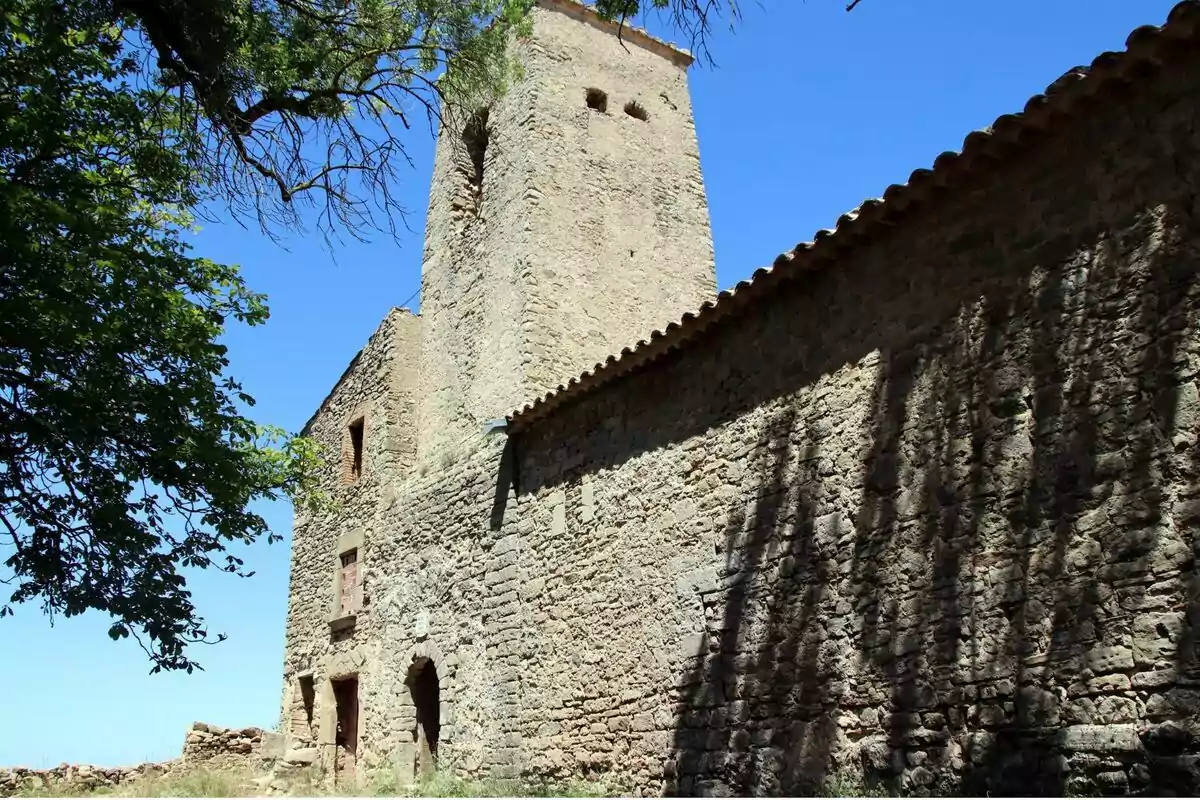 Una antiga construcció de pedra amb una torre i un arbre al costat sota un cel clar.