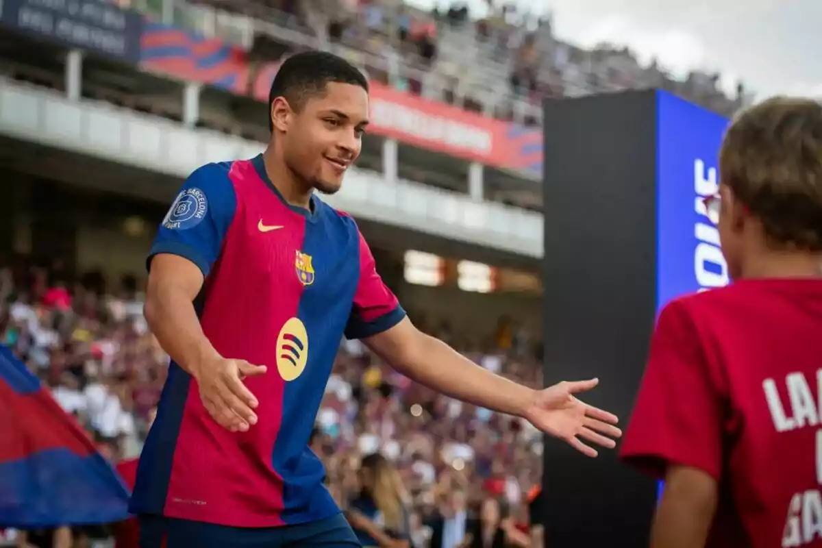 Un jugador de fútbol con la camiseta del FC Barcelona se acerca a un aficionado en un estadio lleno de espectadores.