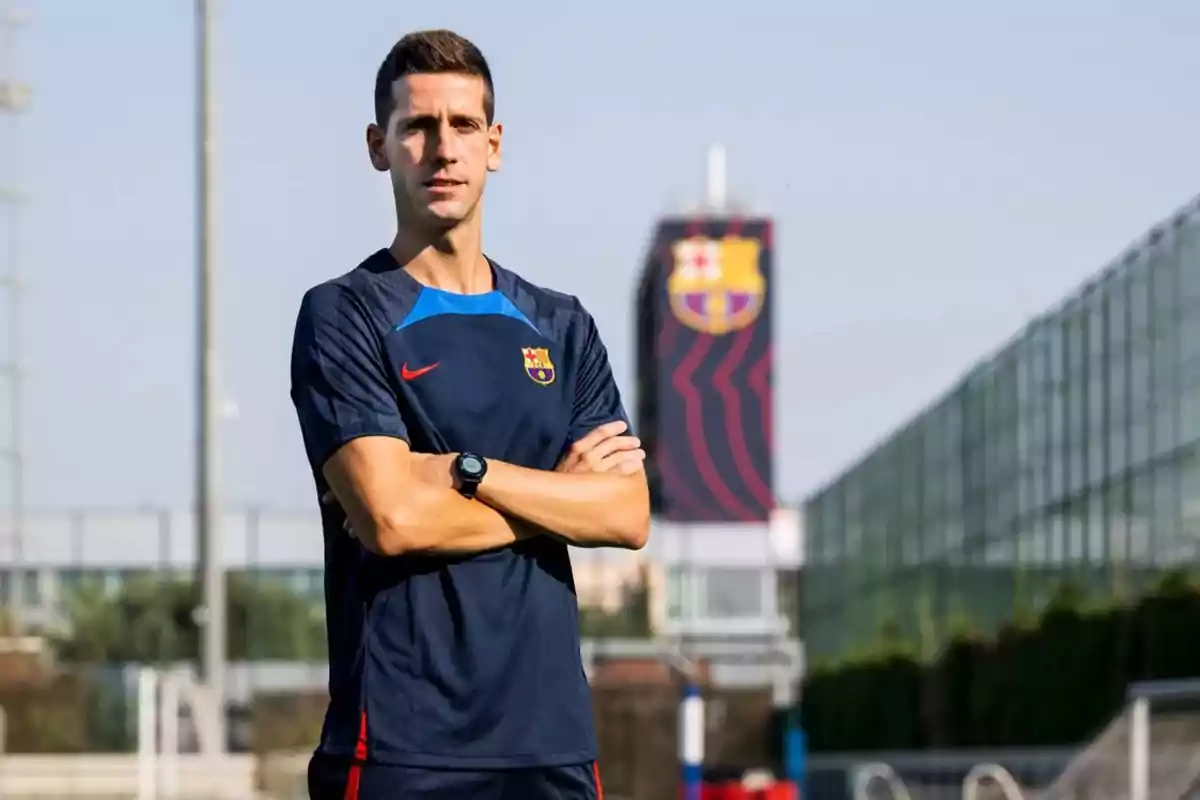 Un home amb uniforme del FC Barcelona posant els braços plegats en un camp d'entrenament.