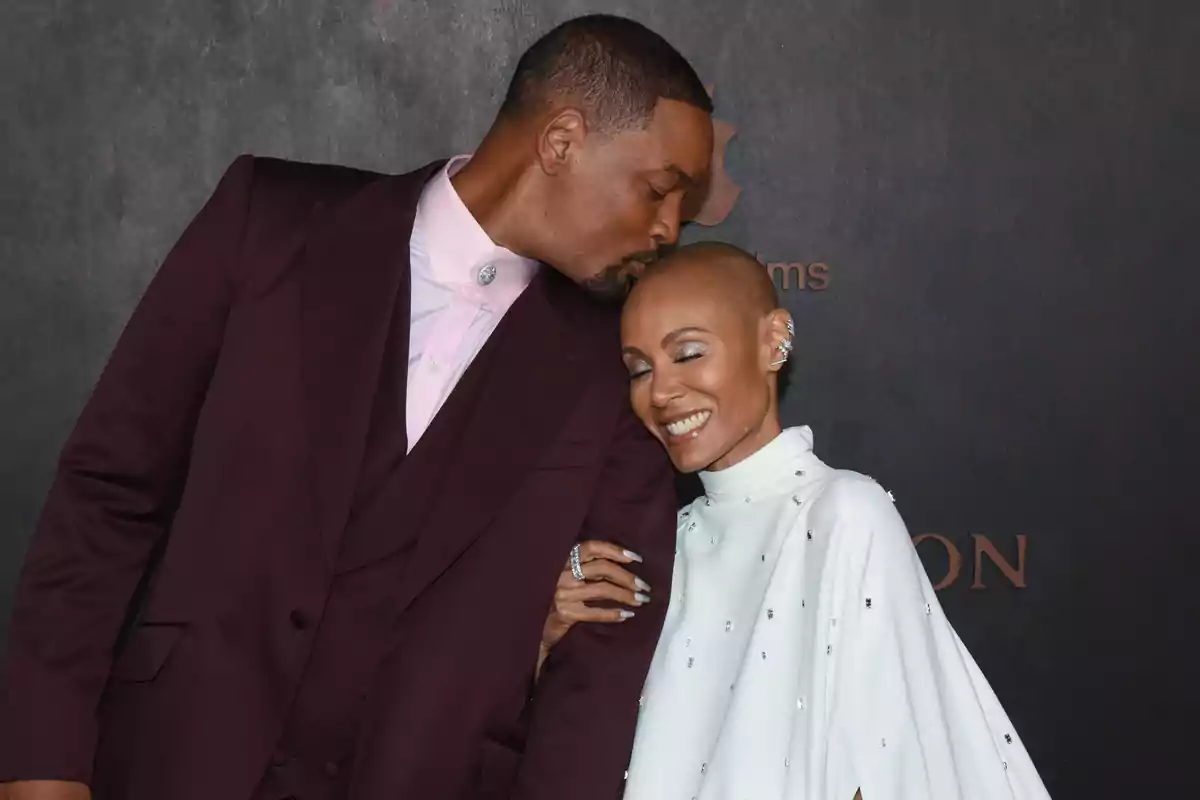 Will Smith amb vestit vermell besant el cap de Jada Pinkett amb un vestit blanc. Will Smith amb vestit vermell besant el cap de Jada Pinkett amb un vestit blanc.